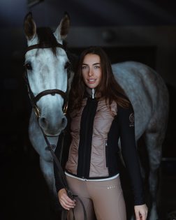 Jazdecká hybridná bunda čierno-hnedá – modelka s bielym koňom v stajni